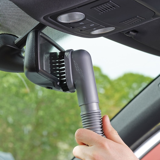BLACKDECKER ADV1200 handheld vacuum brush cleaning a car rearview mirror, close-up angle.