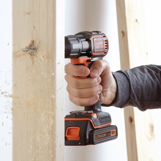 BLACK+DECKER ASD18KB cordless drill in use, drilling through wood, side angle view.
