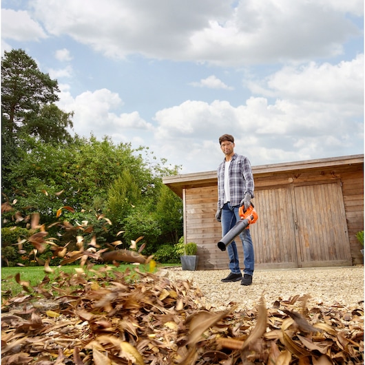 Photo of BLACKDECKER BCBL200L25 leaf blower in use outside, blowing leaves near a wooden shed.