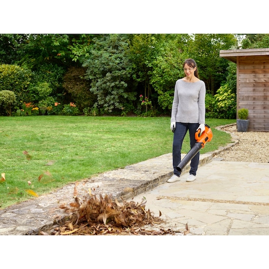 BLACKDECKER BCBL200L25 leaf blower in use outdoors, orange and black design, garden background.