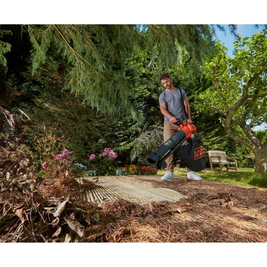 BLACK+DECKER BCBLV3625L1 leaf blower with collection bag used in garden, blowing dry leaves from patio.