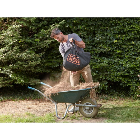 BLACK+DECKER BCBLV3625L1 garden vacuum debris bag being emptied into a wheelbarrow outdoors.