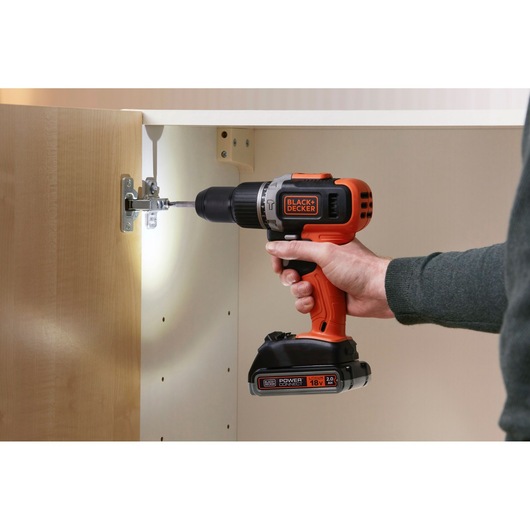 BLACKDECKER cordless drill BCD003D2AMB in use assembling a cabinet, orange and black color, side view.