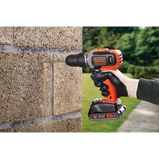 BLACK+DECKER BCD003D2AMB cordless drill in use drilling into outdoor stone wall, close-up view.