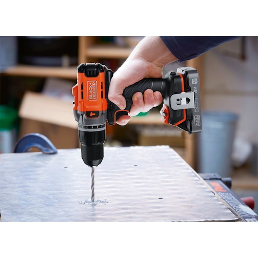 BLACK+DECKER BCD383D1 cordless drill being used to drill metal sheet, close-up in workshop setting.
