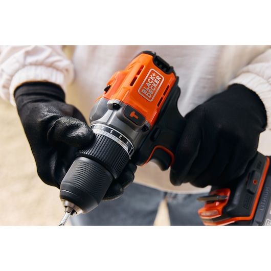 Close-up photo of BLACK+DECKER BCD383D1 cordless drill being adjusted by hands in black gloves.