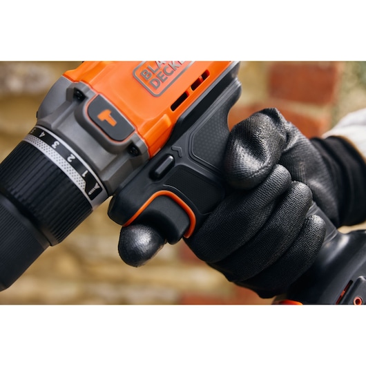 Close-up photo of BLACK+DECKER BCD383D1 cordless drill held by a gloved hand, showing grip and trigger details.