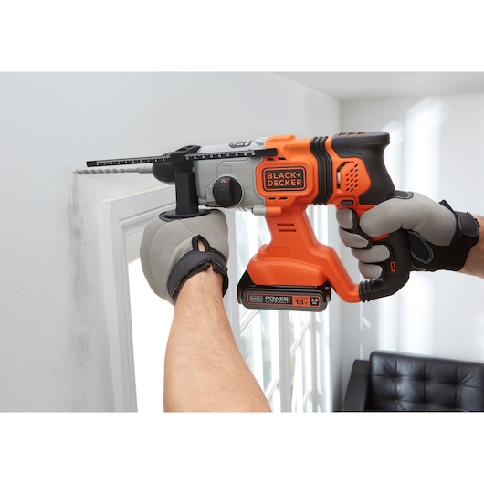 Photo of BLACK+DECKER BCD900B cordless hammer drill in use, orange and black design, drilling into a white wall.