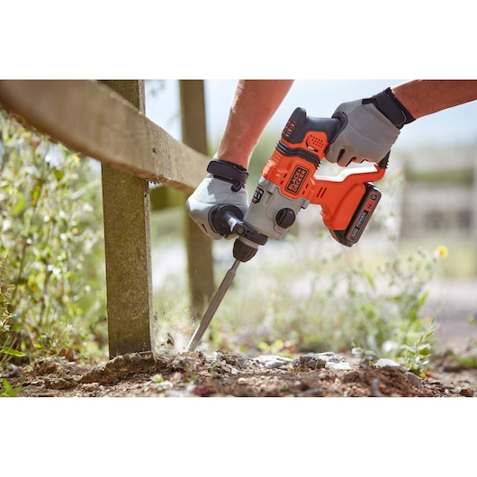 BLACKDECKER BCD900B cordless rotary hammer drill with chisel bit, used outdoors near a wooden post.
