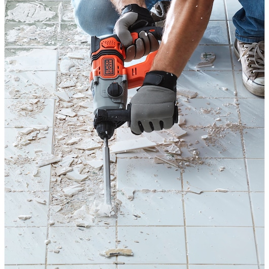 BLACK+DECKER BCD900D1S rotary hammer used to remove tiles on a white tiled floor, close-up view.