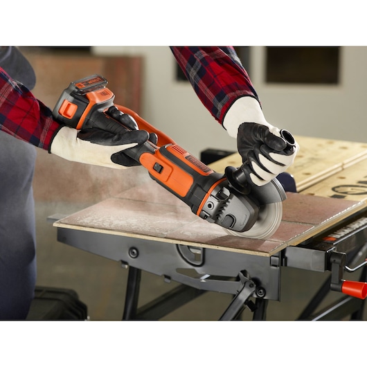 BLACKDECKER BCG720N angle grinder in use, cutting tile, close-up view, worker wearing gloves.