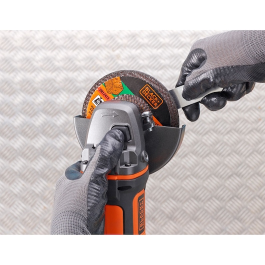 Photo of BLACKDECKER BCG720N angle grinder being adjusted with gloved hands, close-up on tool and disc.