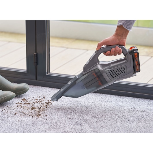BLACKDECKER BCHV001C1 handheld vacuum cleaning dirt from carpet near a window.