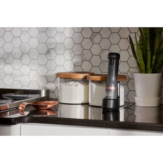Photo of BLACK+DECKER BCKM1011KGF cordless milk frother on kitchen counter near storage jars and a plant.