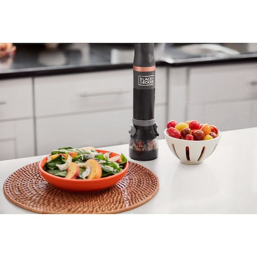 Photo of BLACK+DECKER BCKM1011KGF black electric pepper grinder on kitchen counter with salad and tomatoes.