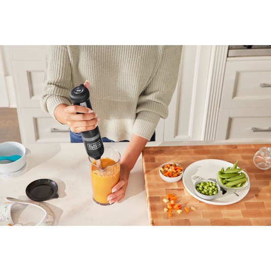 Photo of BLACKDECKER BCKM1012KB hand blender mixing orange smoothie in a kitchen setting.