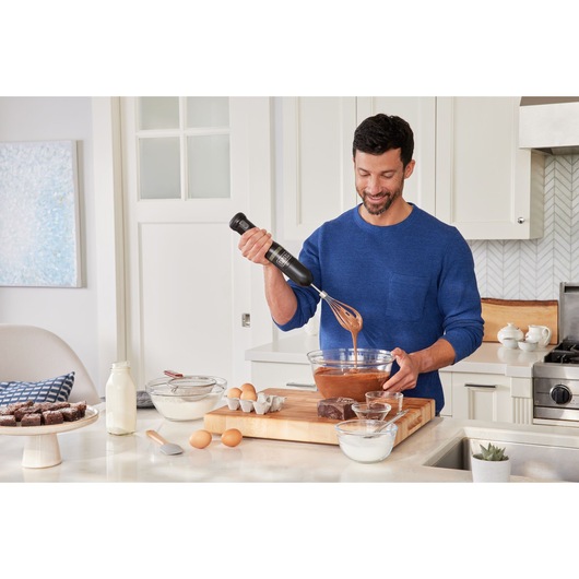 BLACKDECKER BCKM1012KB hand mixer used to mix chocolate batter in a glass bowl in a kitchen setting.