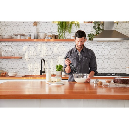 Black+Decker hand mixer BCKM1012KB used in a kitchen, mixing batter in a glass bowl on a wooden counter.