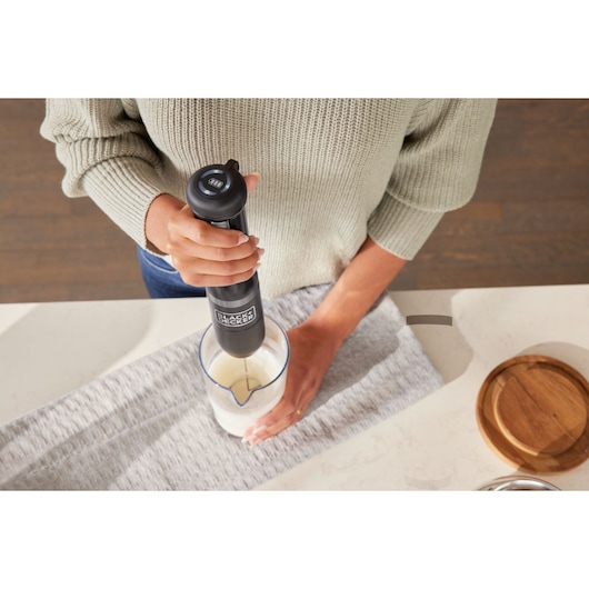 Photo of BLACKDECKER hand blender BCKM1016KSB mixing ingredients in a clear measuring cup on a kitchen counter.