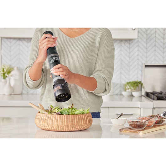 BLACK+DECKER BCKM1016KSB electric grinder used to season salad in a wooden bowl in modern kitchen.