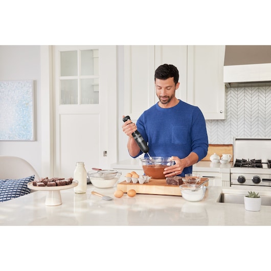 BLACKDECKER BCKM1016KSB hand mixer used to mix batter in a kitchen setting with baking ingredients visible.