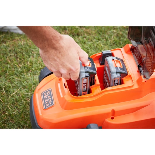 Photo of a BLACKDECKER BCMW3318N lawn mower with a hand inserting an 18V battery into the orange battery compartment.