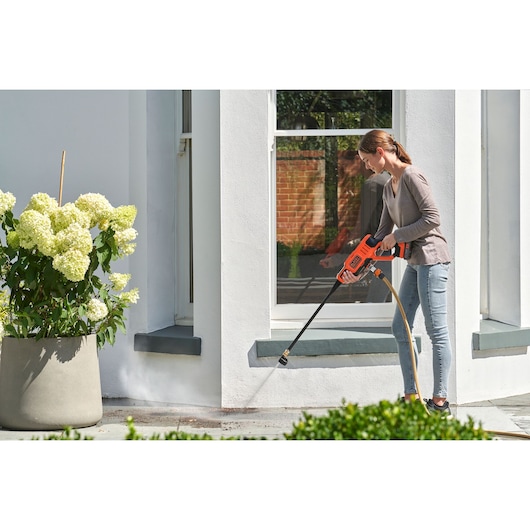 Photography of BLACKDECKER BCPC18D1 pressure washer cleaning outdoor patio near white wall and potted flowers.