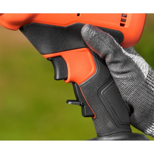 Close-up of BLACK+DECKER BCPP18D1 power tool handle with textured black grip and orange trigger, hand with glove holding.