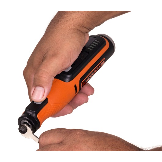 A close-up of hands using a BLACK+DECKER orange cordless rotary tool, with a wrench being applied to adjust a part of the tool.