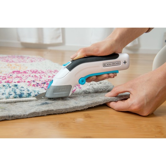 BLACK+DECKER BCSC115 utility cutter with black and blue handle trimming carpet edge, close-up photo.