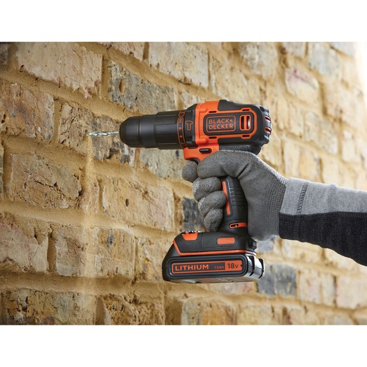BLACKDECKER BDC718AS2F cordless drill in use drilling into brick wall, orange and black design, photography category