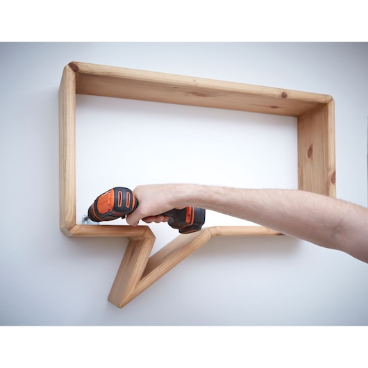 Photo of BLACKDECKER BDCD12 cordless drill in use mounting a wooden shelf on a white wall.