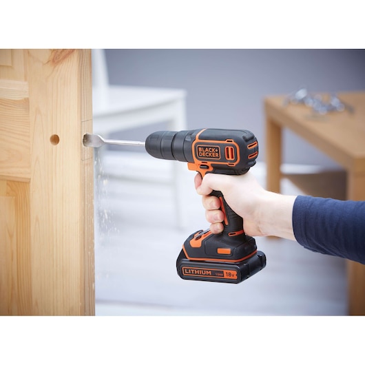 BLACKDECKER BDCD18K cordless drill in use on wooden door, black and orange design, side angle.
