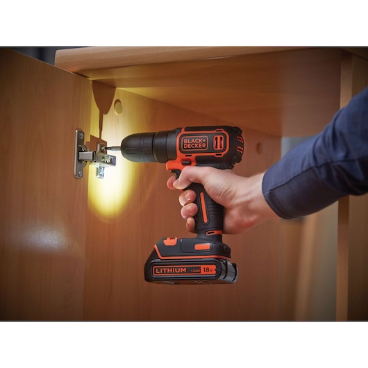 BLACKDECKER BDCD18K cordless drill in use on cabinet hinge, orange and black, handheld side angle.