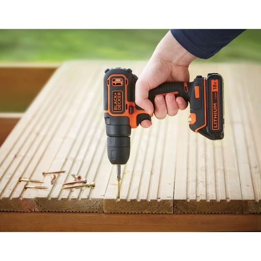 Photo of BLACK+DECKER BDCD18 cordless drill in use on wooden boards, visible screws beside, outdoor setting.