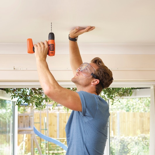 Photography of BLACKDECKER BDCD8K orange cordless drill used to drill into a ceiling indoors.