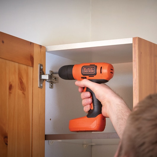 Photo of BLACK+DECKER BDCD8K cordless drill in use on cabinet hinge indoors.