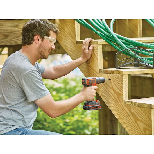 BLACKDECKER BDCDC18 cordless drill used on wooden stairs outdoors.