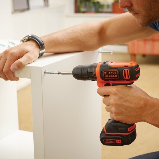 BLACKDECKER BDCDD12B cordless drill used to assemble white furniture indoors.
