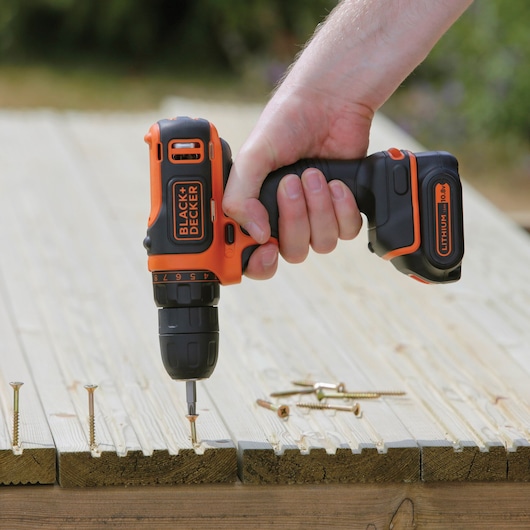 BLACKDECKER BDCDD12B cordless drill used to drive screws into wooden planks outdoors.