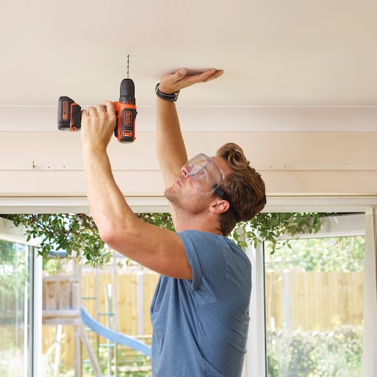 Photo of BLACKDECKER BDCDD12KB cordless drill being used to drill into a ceiling indoors.