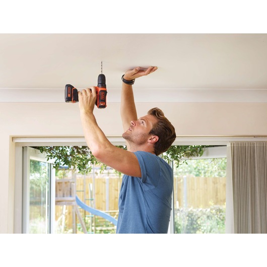 Photo of BLACKDECKER BDCDD12 cordless drill in use drilling into a ceiling indoors.