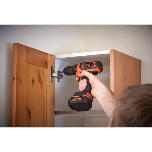 Photo of BLACKDECKER BDCDD12 cordless drill adjusting cabinet hinge, black and orange design, in-use scene.
