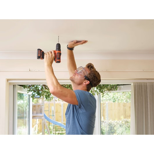 Photo of BLACK+DECKER BDCDD12 cordless drill being used to drill a ceiling indoors.