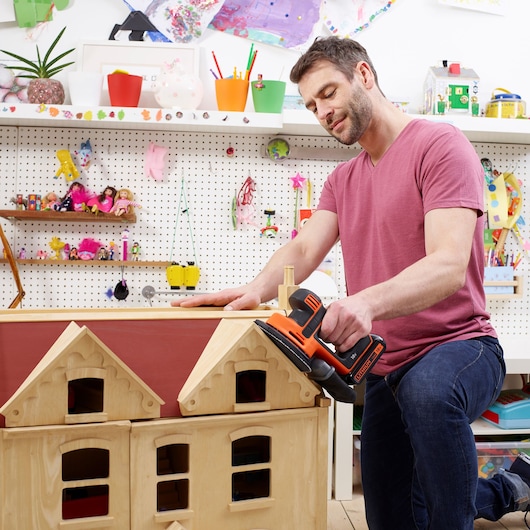 Photo of BLACKDECKER BDCDS18 sander used on wooden dollhouse in colorful workshop setting.