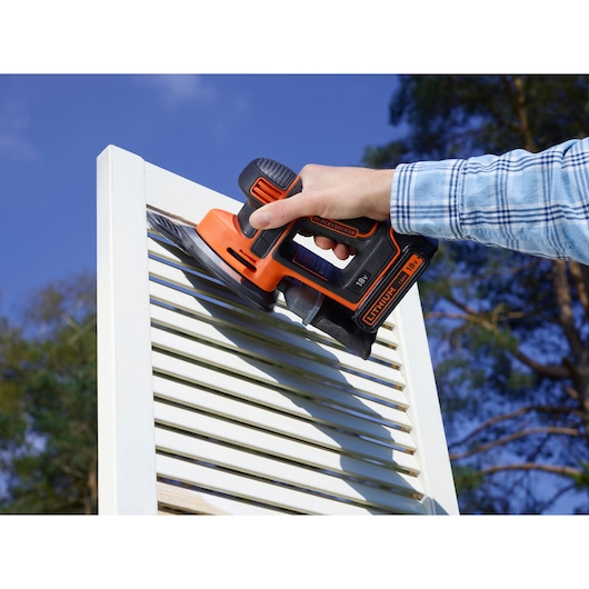 Photo of BLACK+DECKER BDCDS18 cordless sander in use on white shutters, outdoors.