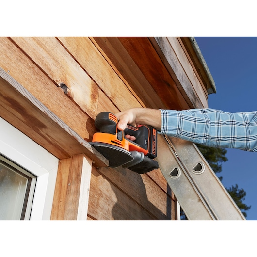 Photo of BLACKDECKER BDCDS18 cordless sander in use on wooden siding outdoors.