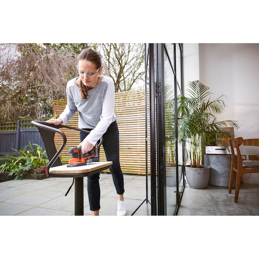 BLACKDECKER BDCDS18 sander used on a chair outdoors, person holding tool near patio door.