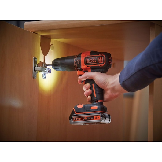 BLACK+DECKER BDCHD18KB2 cordless drill being used to install a hinge on a wooden cabinet.