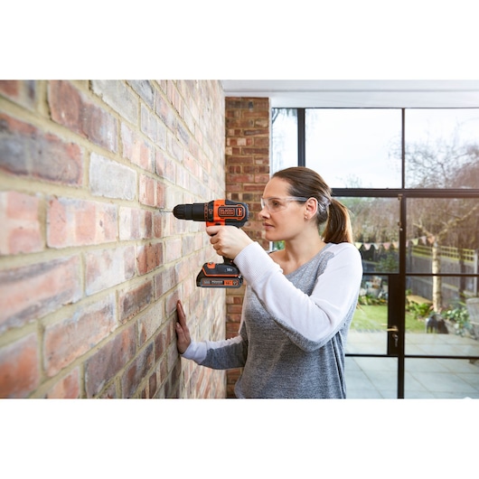 BLACKDECKER BDCHD18KB2 cordless drill in use drilling a brick wall indoors.